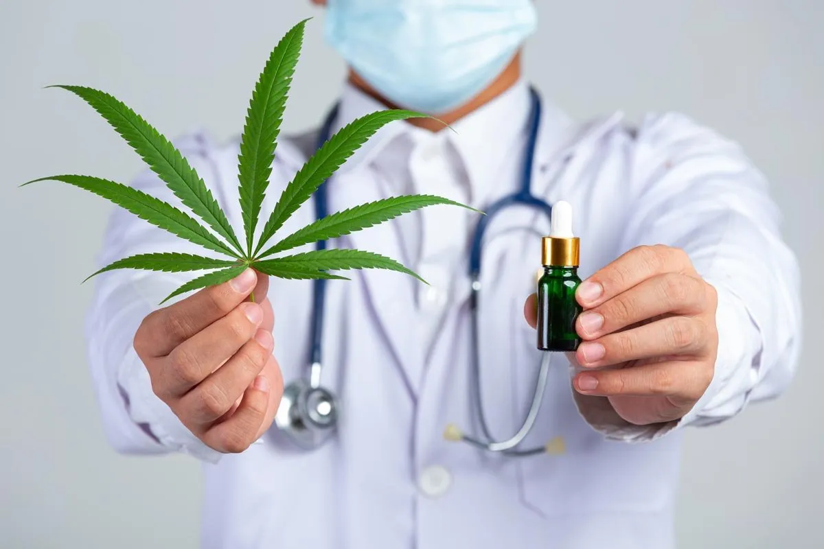 Person in medical clothing holding a leaf and dropper bottle